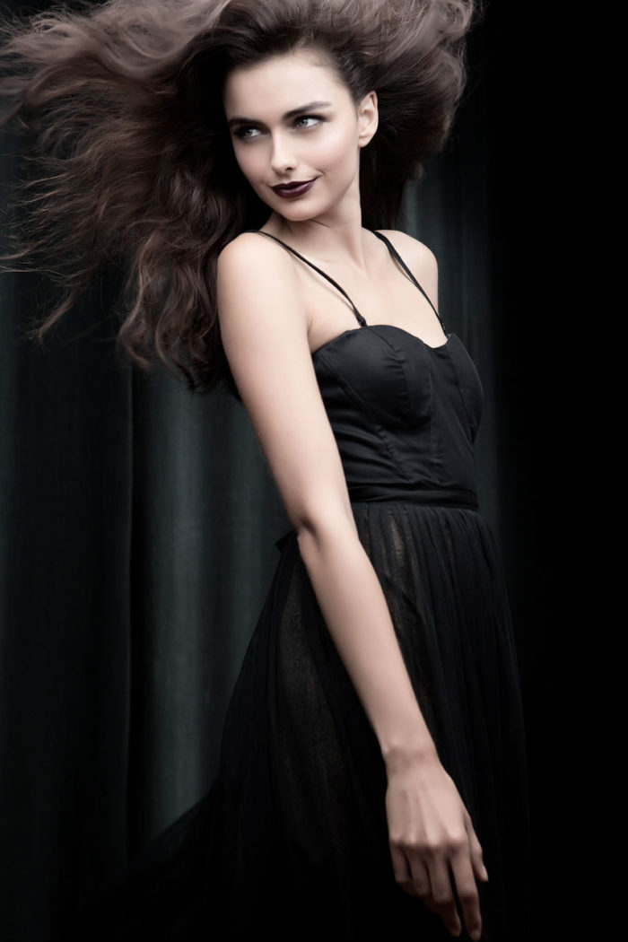 Dark haired fashion model in black dress with dark makeup and purple lipstick by Kyrsten Bryant