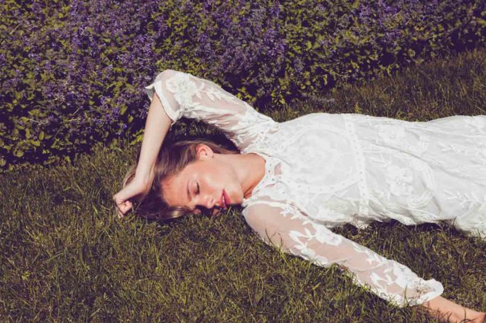 Fashion model lying in grass in white dress with pink lipstick and glowing makeup by Kyrsten Bryant